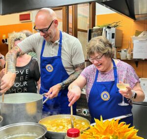 Image of a cooking class with guests: A man and a woman stirring risotto and chicken in a kitchen, preparing a meal together.